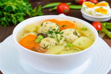 Light dietary soup with meat balls, vegetables, fusilli and boiled eggs on a dark wooden table. Useful lunch.