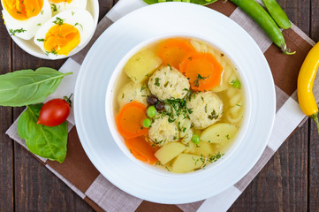 Light dietary soup with meat balls, vegetables, fusilli and boiled eggs on a dark wooden table. Useful lunch. The top view