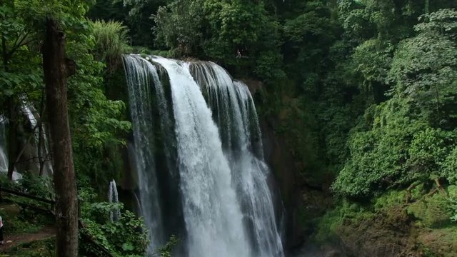 Tilt down of beautiful Pulhapanzak waterfall in Honduras. Man zip lines over waterfall