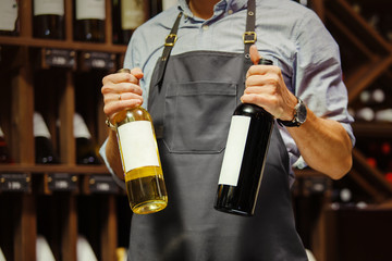 Young sommelier holding bottle of red wine in cellar