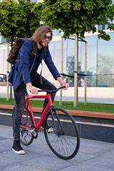 A man with backpack sits on the red fixed bicycle.