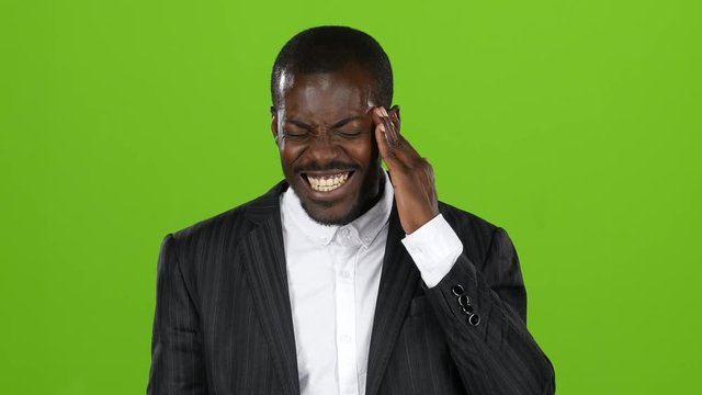 Afroamerican guy in costume experiences a severe headache. Green screen
