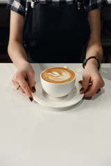 Female hands put on a white table a cappuccino Cup with drawing, photos free background bottom text