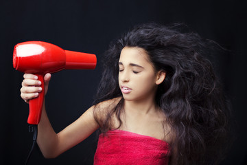 Girl wearing a towel drying her hair with a hairdryer  on black background