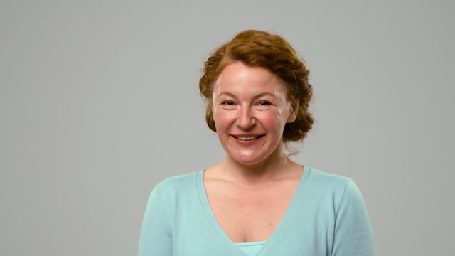 Foxy haired actress showing tricky smile. Mid aged woman with flirtation smile in the studio on white background, covering mouth with palm.