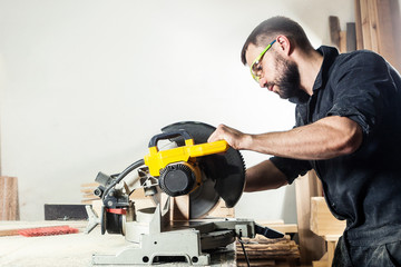 Young man builder carpenter sawing board with circular saw in workshop