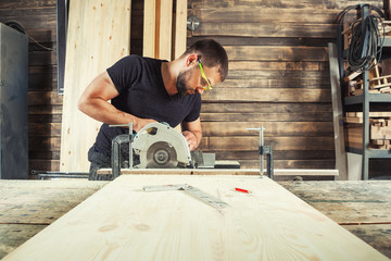 A man builder saws a board with a circular saw in the workshop