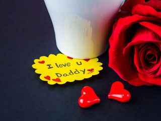 Father's day concept. I LOVE YOU DADY message with red rose, two red heart and gift on black background