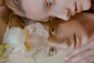 portrait of the young blonde attractive woman with the fashion alien gold make up laying with the iris flowers on the mirror 