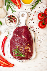 Raw meat with herbs, spices and seasoning on white wooden background, ingredients for cooking, top view. Beef meat on cutting board, copy space