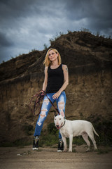 Obraz na płótnie Canvas Brutal, daring girl with a fighting dog breed of bull terrier on the background of a rock