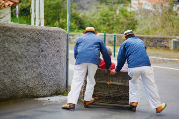 Toboggan riders moving cane sledge downhill on the streets of Funchal, Madeira island