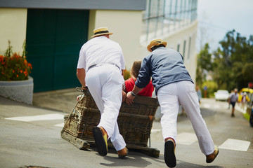 Toboggan riders moving cane sledge downhill on the streets of Funchal, Madeira island - obrazy, fototapety, plakaty