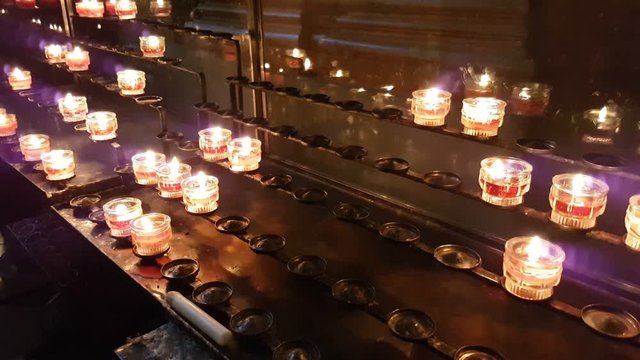 Numerous Christian Catholic votive candles being lit in some cathedral installed on some metal racks. They glimmer and remind about some eternal things, including the impermanence of our life