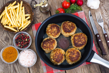 Fries on wooden plate and fried meat patties in frying pan