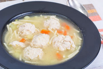 Soup with noodles and meatballs in ablack plate