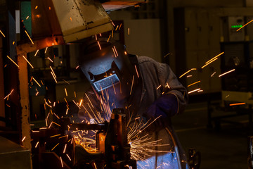 Worker is welding automotive part in car factory 