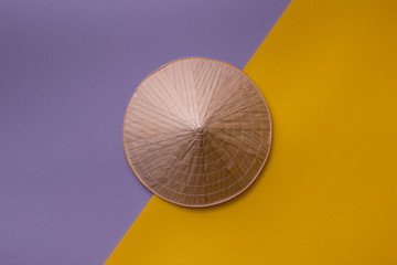 Summer background: Asian conic straw hat on creative, purple and yellow background. Top view, flat lay.