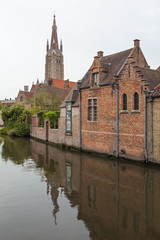 Fototapeta premium Scenic old red brickwork buildings on the canal with Church Our Lady tower in the background in medieval neighborhood of Bruges (Brugge), Belgium