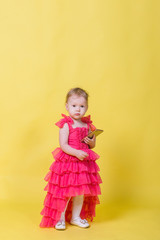 Girl toddler in a pink dress on a yellow background holding a smartphone and looking at the camera