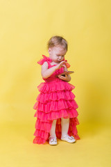 Girl toddler in a pink dress on a yellow background holding a smartphone