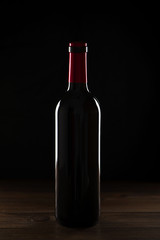 Fototapeta na wymiar Bottle of wine on wooden table. Backlighting. Vertical studio shot.