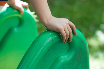 Die Hände eines Kleinkindes welches sich an einer grünen Rutsche festhalten.