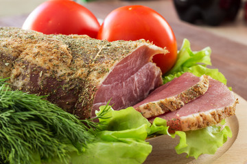 Slices of smoked meat with lettuce and tomato on a wooden board. Selective focus. Horizontal.