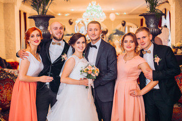 Happy newlyweds with bridesmaids and groomsman posing in hotel reception hall.