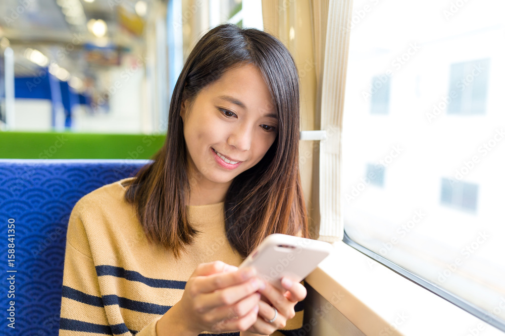 Wall mural Woman sending sms on mobile phone in train