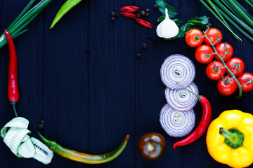 Top view on table with various tomatoes, onion slices, chili peppers, herbs and spices frame over black wooden background, copy space