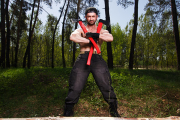 Strong healthy adult ripped man lumberjack worker standing in the forest with two big crossed axes