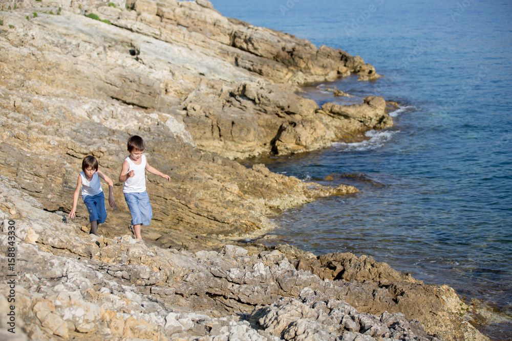 Sticker Two children, boys, running on rocks on the shore of the sea