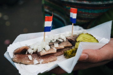 A hand holds a traditional Dutch delicacy of herring with gherkins and onions.