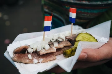 Foto auf Acrylglas Antireflex A hand holds a traditional Dutch delicacy of herring with gherkins and onions. © bortnikau