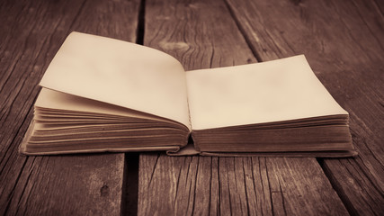 Old opened antique book on the wooden table with blank page. Retro toned.