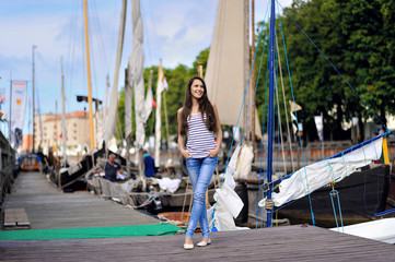 A young smiling woman stands on a pier on the background of the city and boats