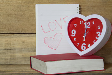 red clock shape like heart and red book and text love in notebook