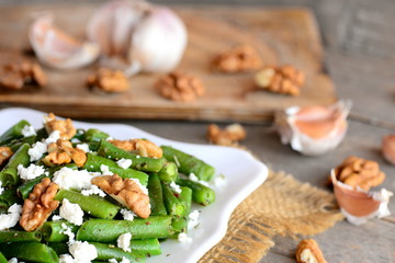 Healthy green beans salad with balsamic dressing. Warm green bean salad with cottage cheese, walnuts, garlic and spices on a plate and an old wooden table. Side dish or veggie main dish