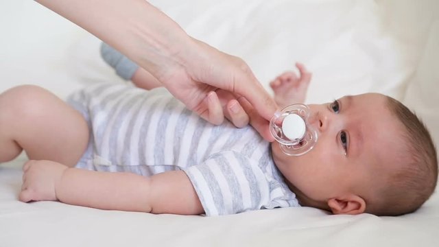 mother gives infant son a pacifier lying in white bed