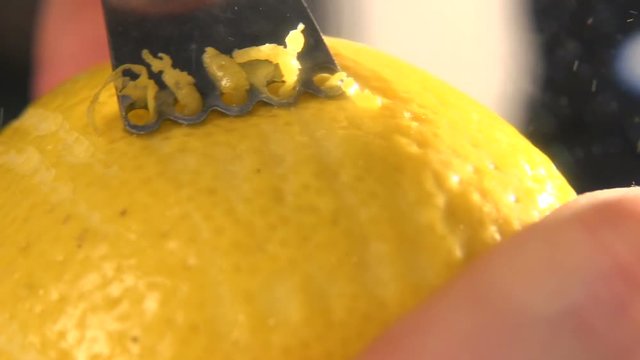 restaurant chef rubbing a lemon peel on a grater in restaurant kitchen. Lemon zest being grated and added to ingredients. Peeling lemon skin. nutrition and wellness. Health food. Slow motion. Close up