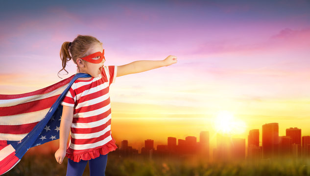 Little Girl Superhero Of Usa With Cityscape At Sunset
