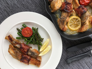 Fillets of carp roasted with bacon, garlic, lemon, asparagus and tomatoes. Top view.