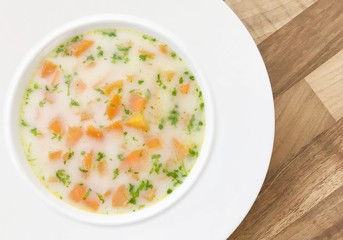 Vegetable carrot soup with cream and green herbs. Wooden background. Top view.