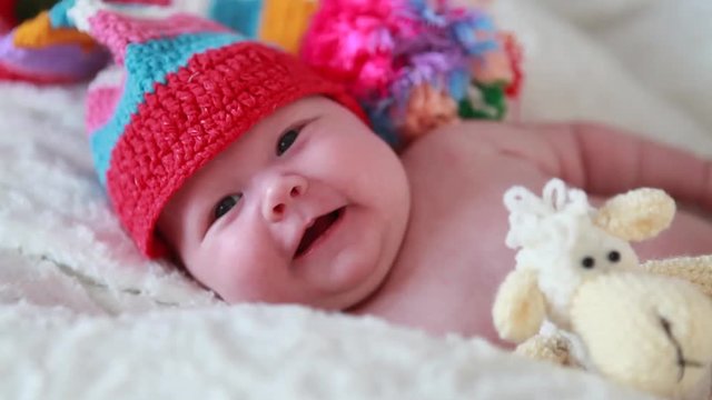 Two-month old girl in a red hat, lying on the bed looking at the camera