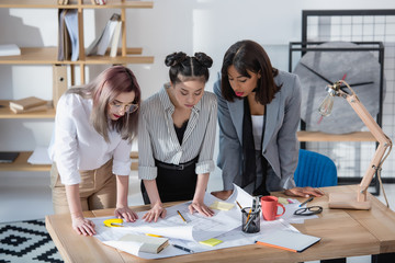 young multiethnic designers looking at blueprints while standing in office