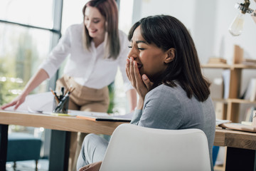 Young african american businesswoman laughing at colleague working behind