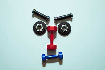 Top view of various dumbbells and weight plates in shape of serious face