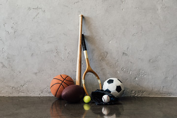 Close-up view of various balls and sports equipment near grey wall - Powered by Adobe