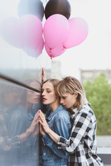 young sensual lesbian couple embracing and holding air balloons outdoors